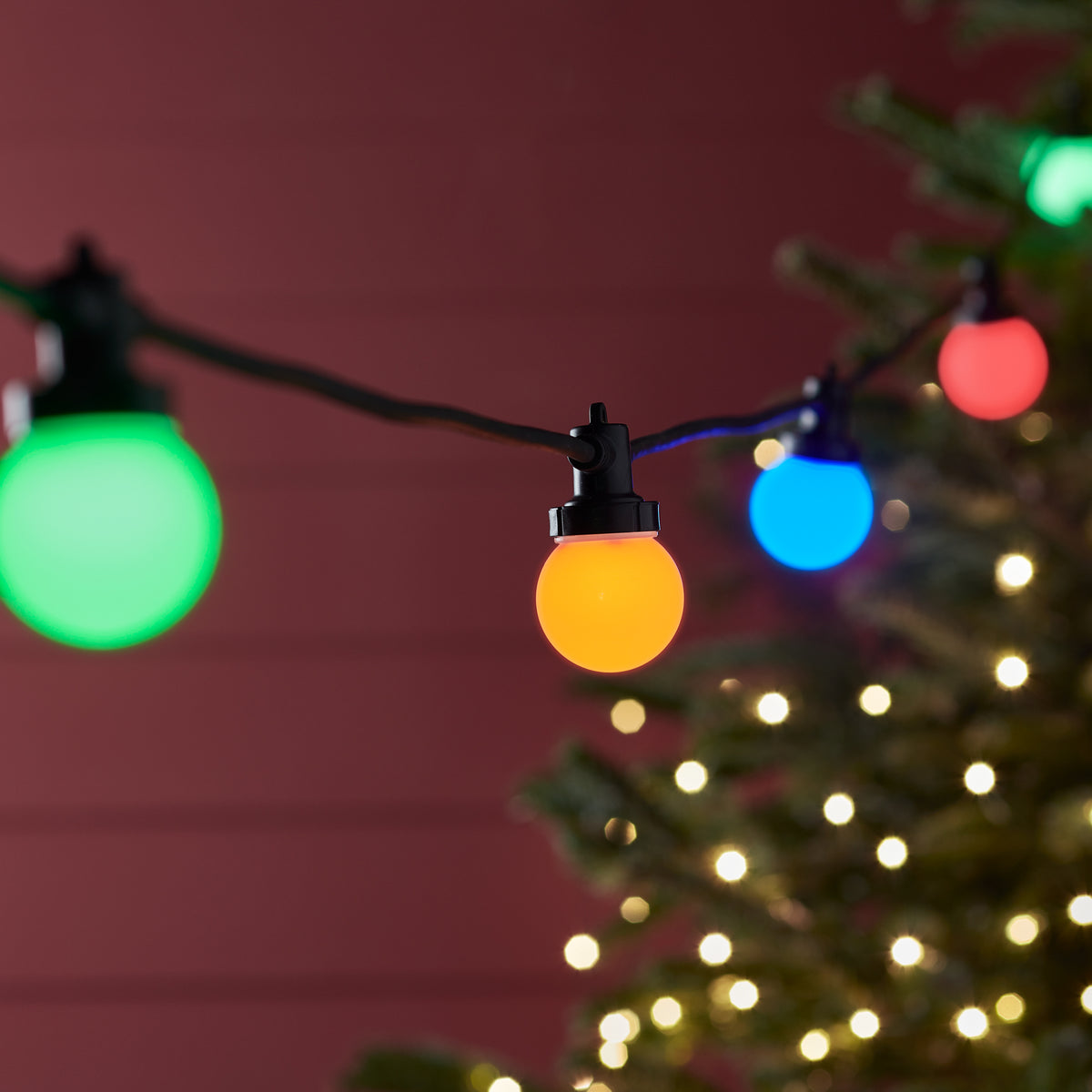 Bunte LED-Glühbirnen der Pro Connect Lichterkette vor rotem Hintergrund mit Lichterglanz
