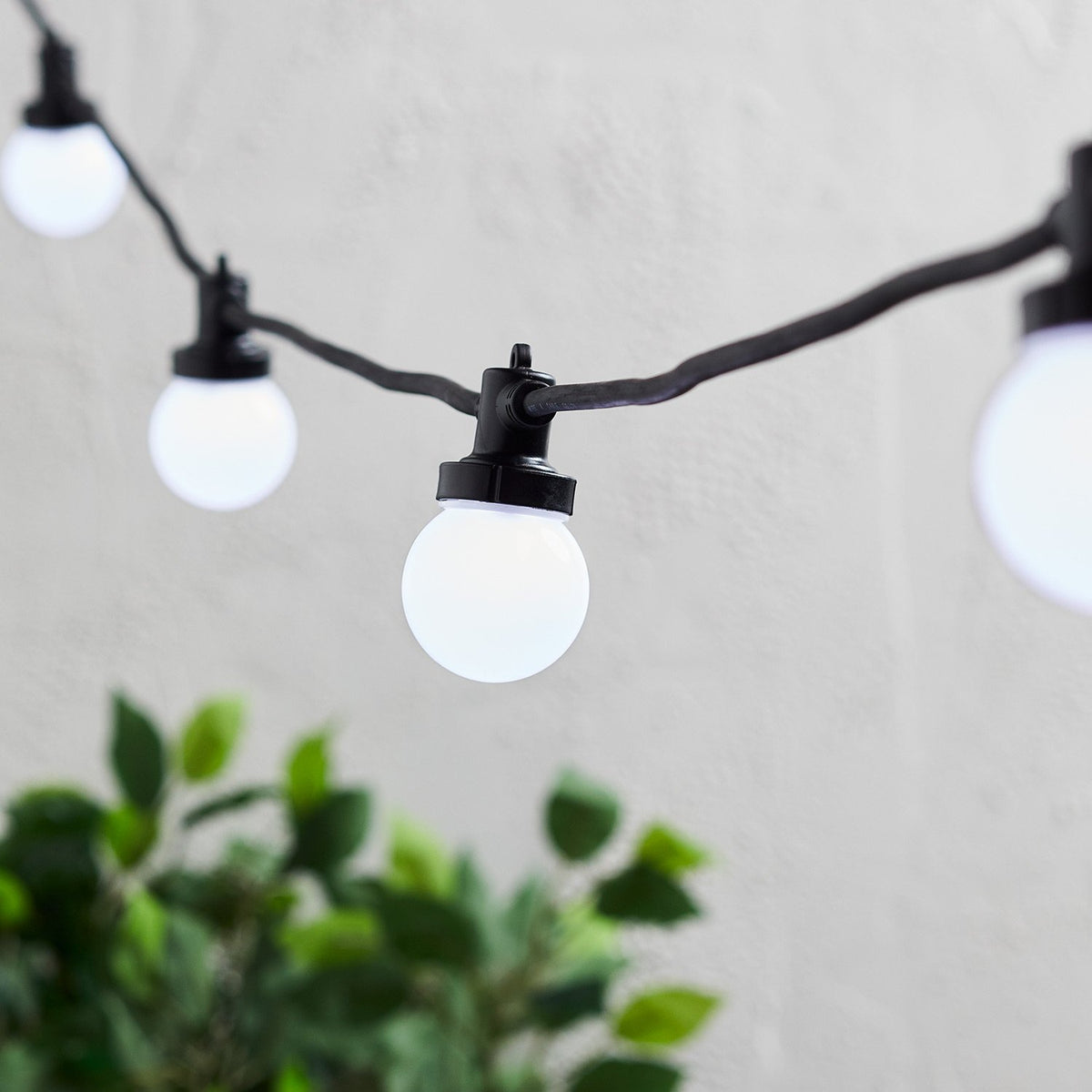 Nahaufnahme weiße LED-Glühbirnen an schwarzem Kabel vor weißer Wand