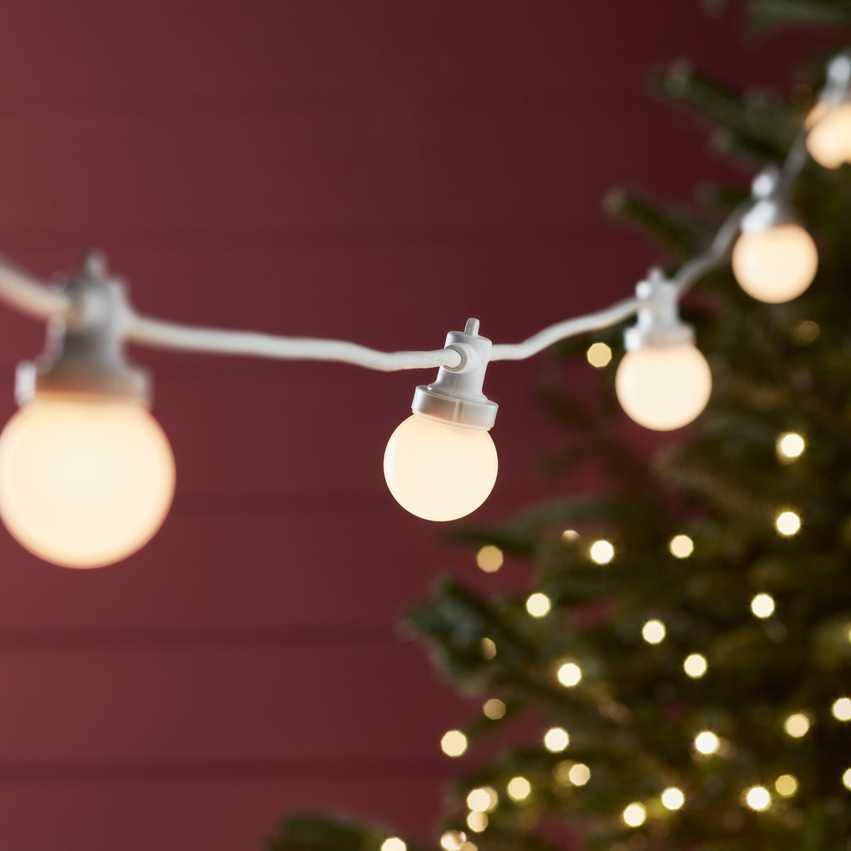 Detailaufnahme von warmweißen LED-Glühbirnen an weißem Kabel vor rotem Hintergrund