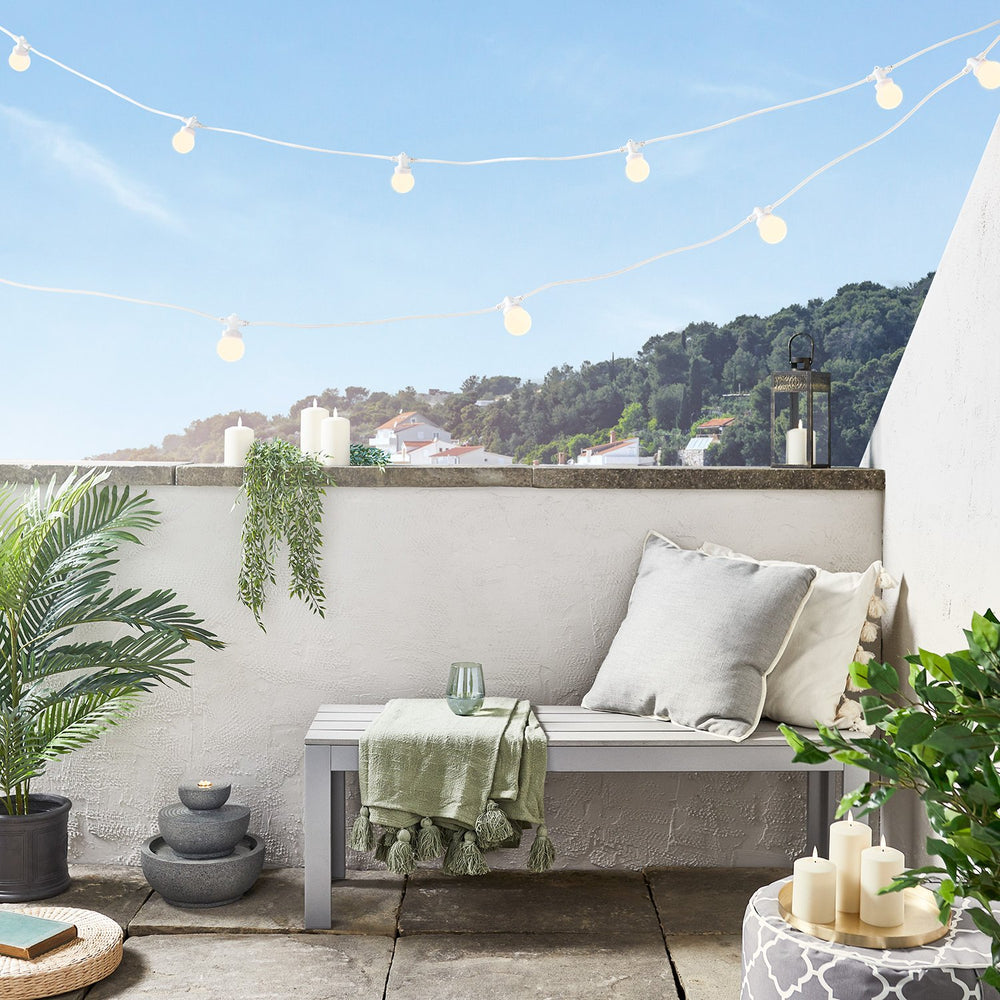 Weiße Lichterkette mit warmweißen Glühbirnen über Balkon mit Bank und Pflanzen