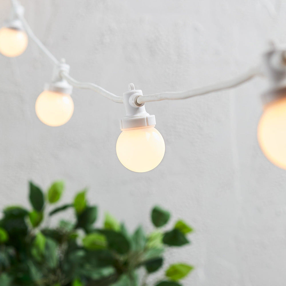 Nahaufnahme einer warmweißen LED-Glühbirne an weißem Kabel vor hellem Hintergrund