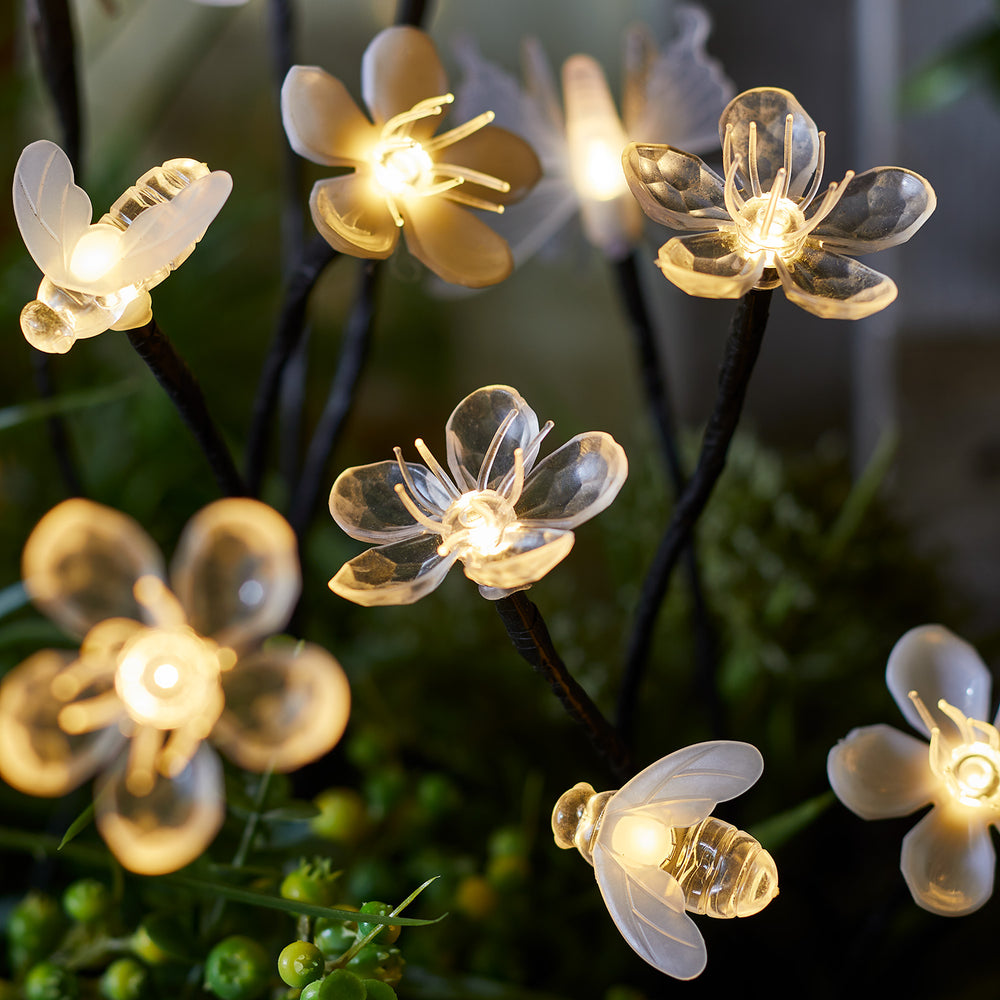 Nahaufnahme von leuchtenden Kunststoffblumen und Bienen mit warmweißen LEDs im Dunkeln