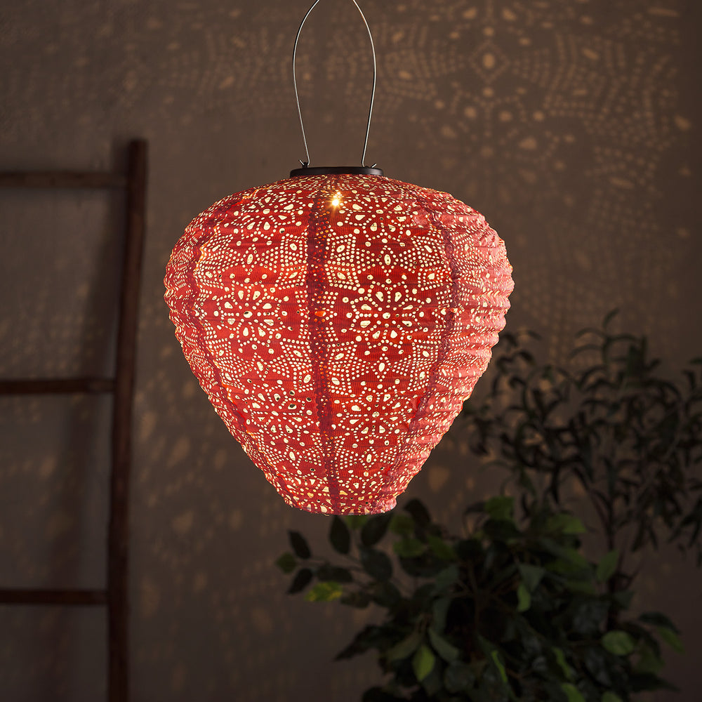 Pinkfarbener Solar-Lampion mit filigranem Cut-Out-Muster leuchtet warmweiß und wirft Muster an Wand