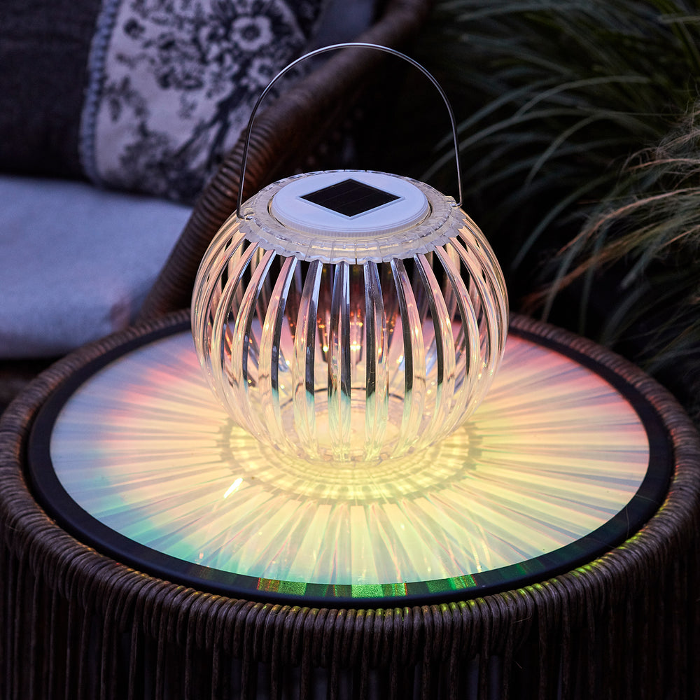 Transparente Solar Hängeleuchte aus Acryl auf Gartentisch bei Dämmerung mit warmem Licht