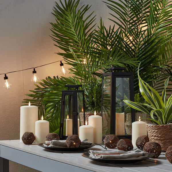 Beleuchtete Lichterkette und Kerzen auf grauem Gartentisch mit grünen Pflanzen