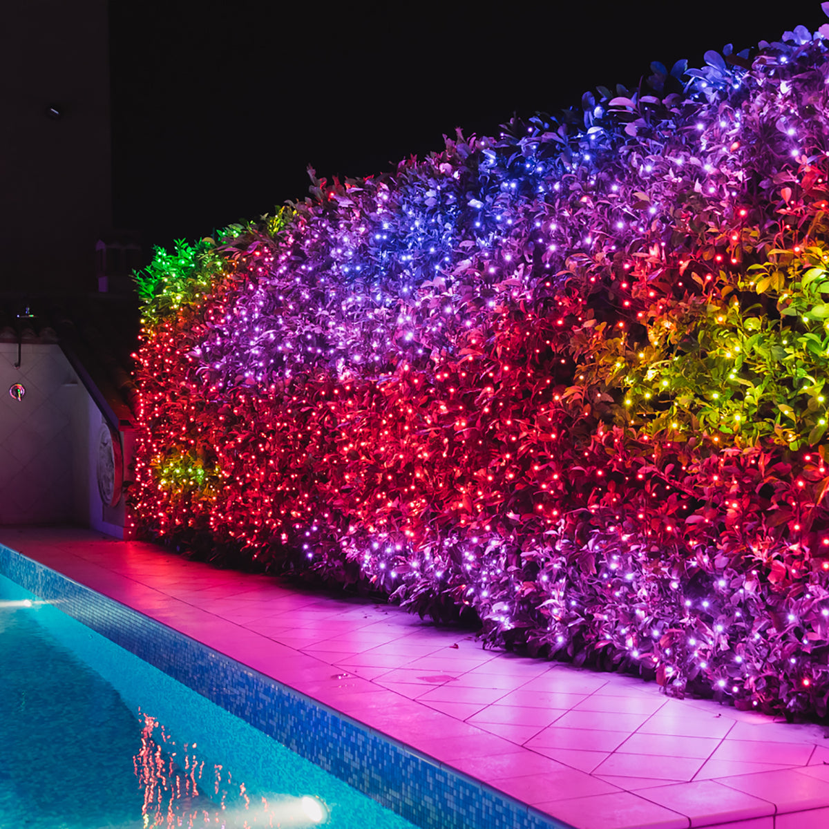 Bunte LED-Lichterkette als Lichtervorhang an einer Hecke neben einem Pool