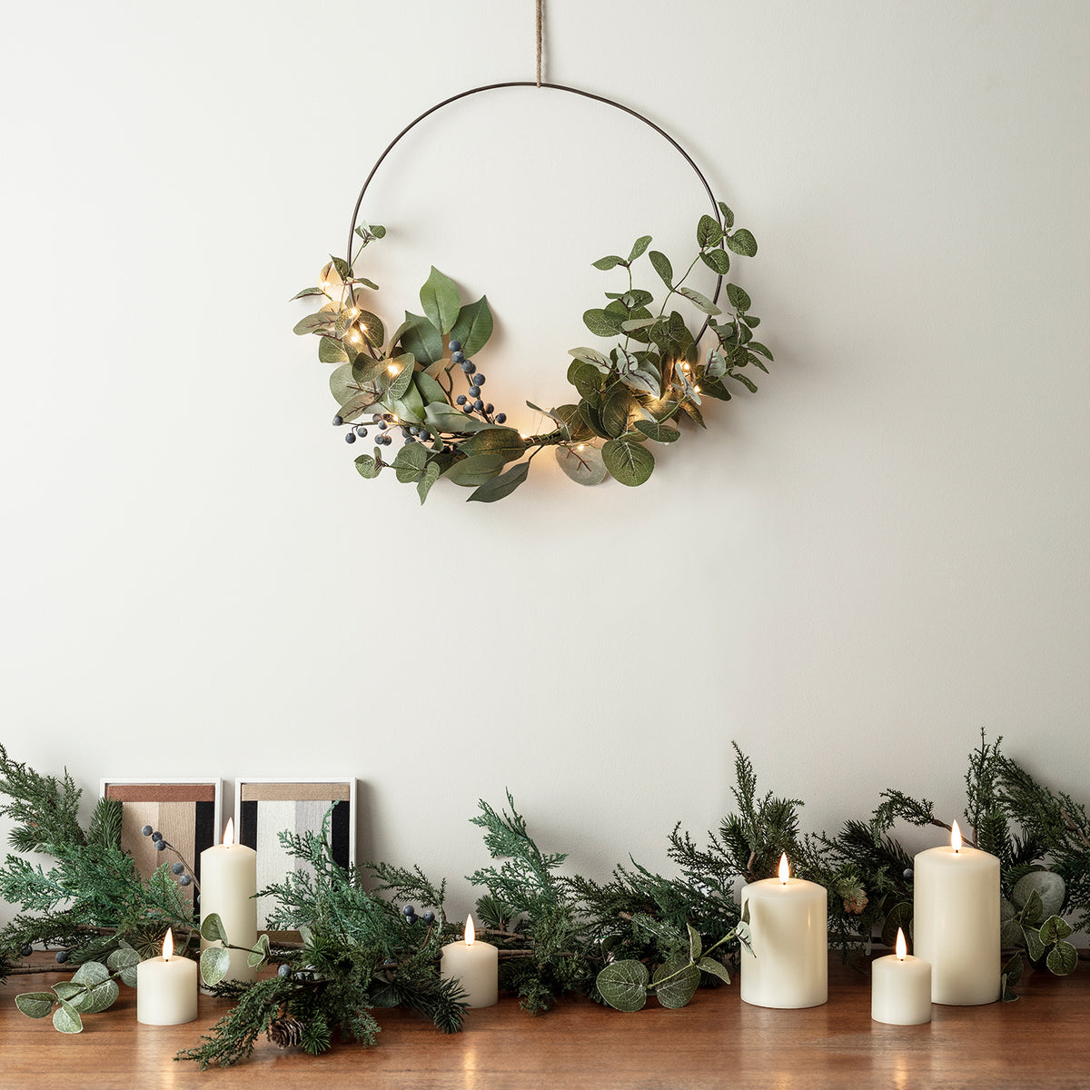 Weihnachtskranz mit grünen Blättern und Beeren, beleuchtet, über Tisch mit Kerzen und Tannengrün