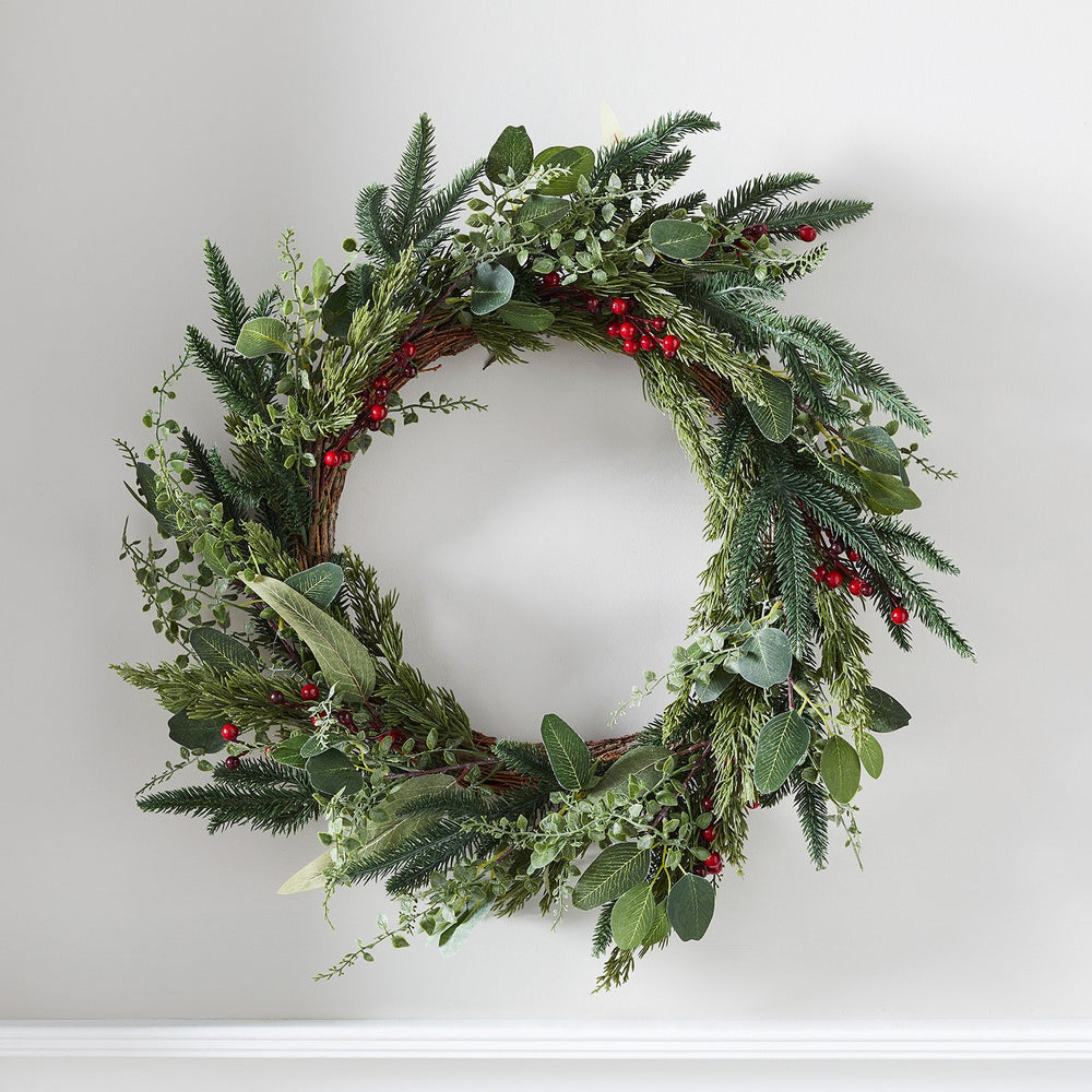 Weihnachtskranz mit grünen Tannenzweigen und roten Beeren an weißer Wand