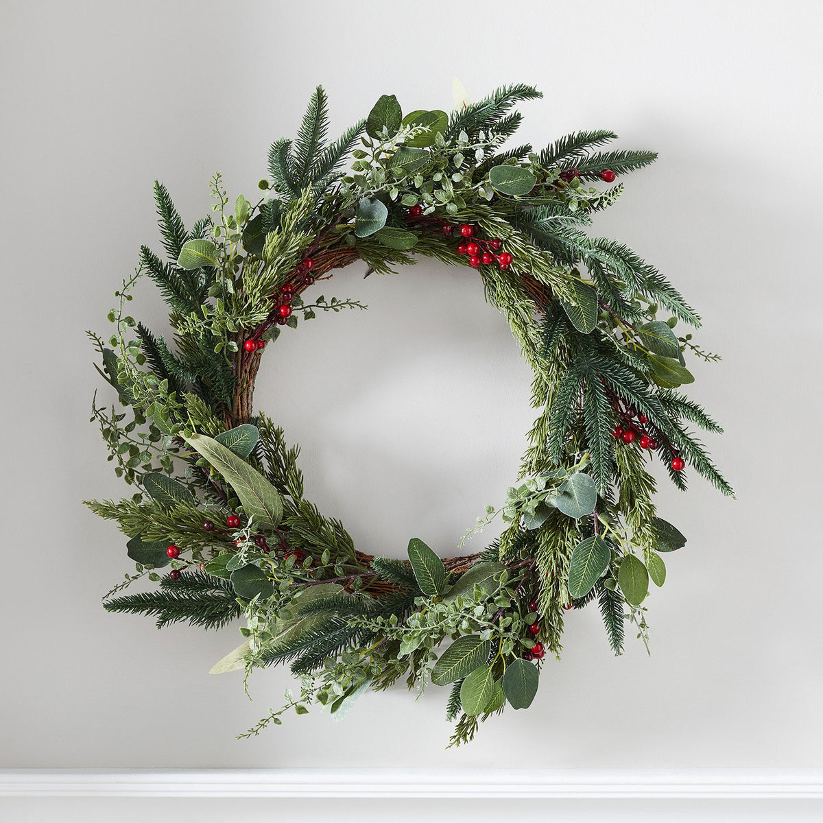 Weihnachtskranz mit grünen Tannenzweigen und roten Beeren an weißer Wand