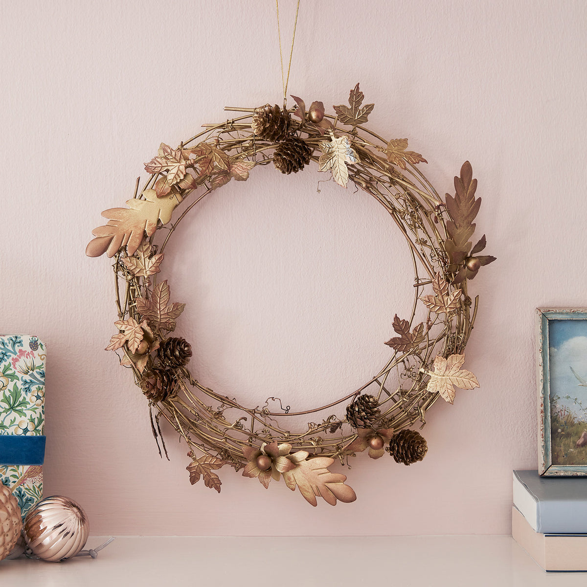Goldener Weihnachtskranz mit Blättern und Zapfen an rosa Wand mit Dekoration