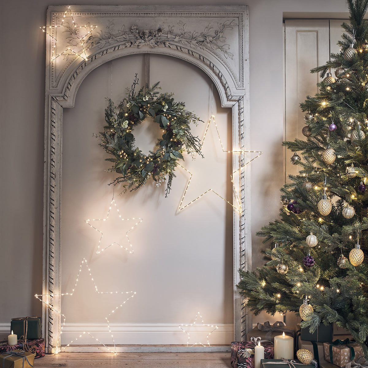 Weihnachtskranz an Wand neben beleuchtetem Weihnachtsbaum und Kerzen auf Holzboden