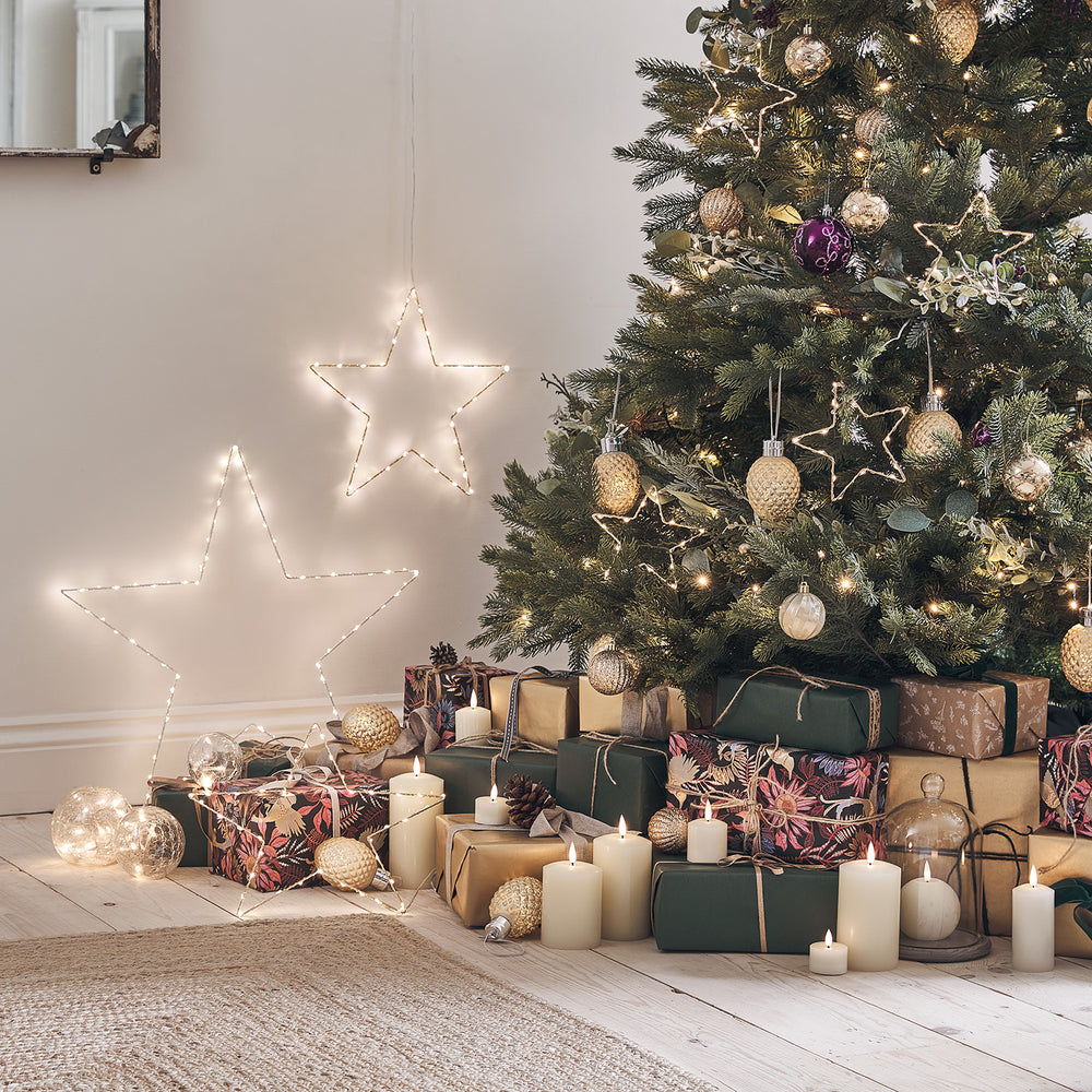 Beleuchtete LED-Sterne neben einem geschmückten Weihnachtsbaum mit Geschenken und Kerzen