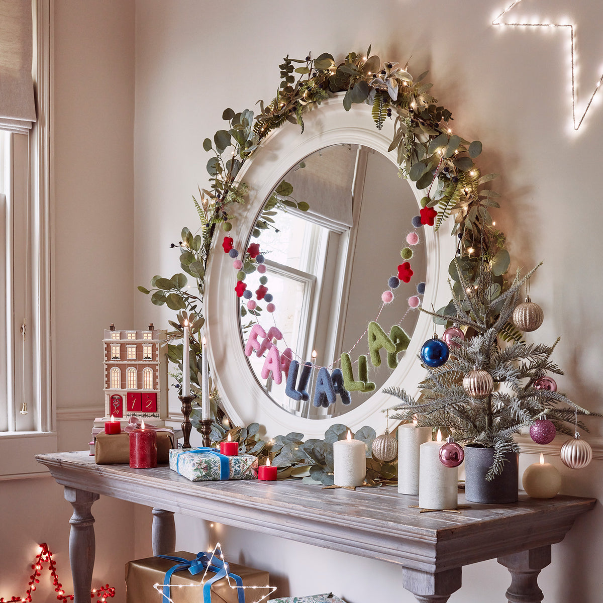Weihnachtsgirlande mit blauen Beeren und Lichterkette über Spiegel und Tisch mit Kerzen und Deko