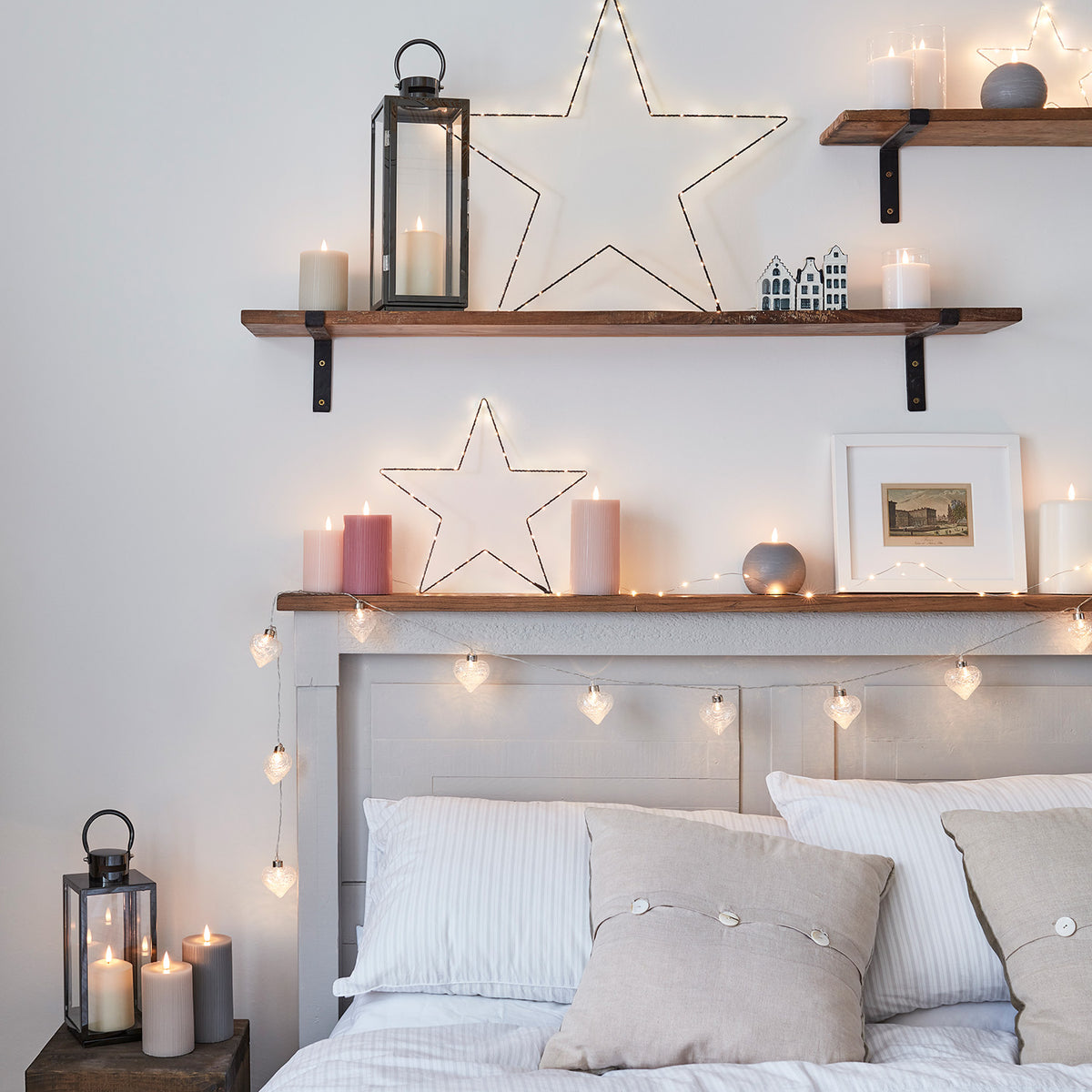 Drei LED-Kerzen in Rosa- und Pastelltönen auf dunklem Holztisch mit Herz-Lichterkette und Kissen