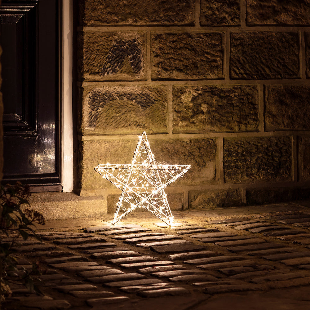 Beleuchteter 35cm LED Stern aus Metall auf Pflastersteinen vor einer Steinwand
