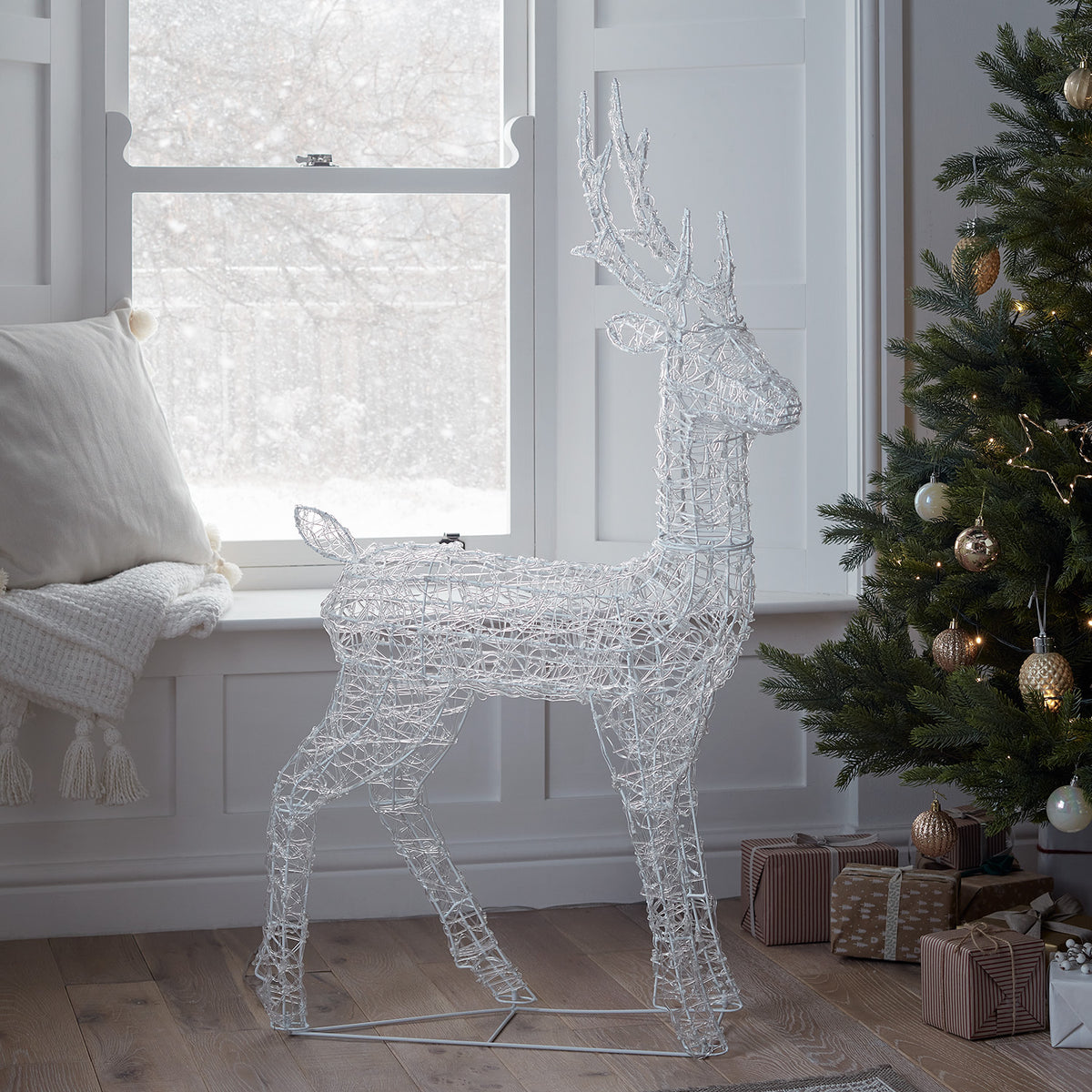 LED-Rentier in Innenraum neben Fenster und Weihnachtsbaum mit Geschenken