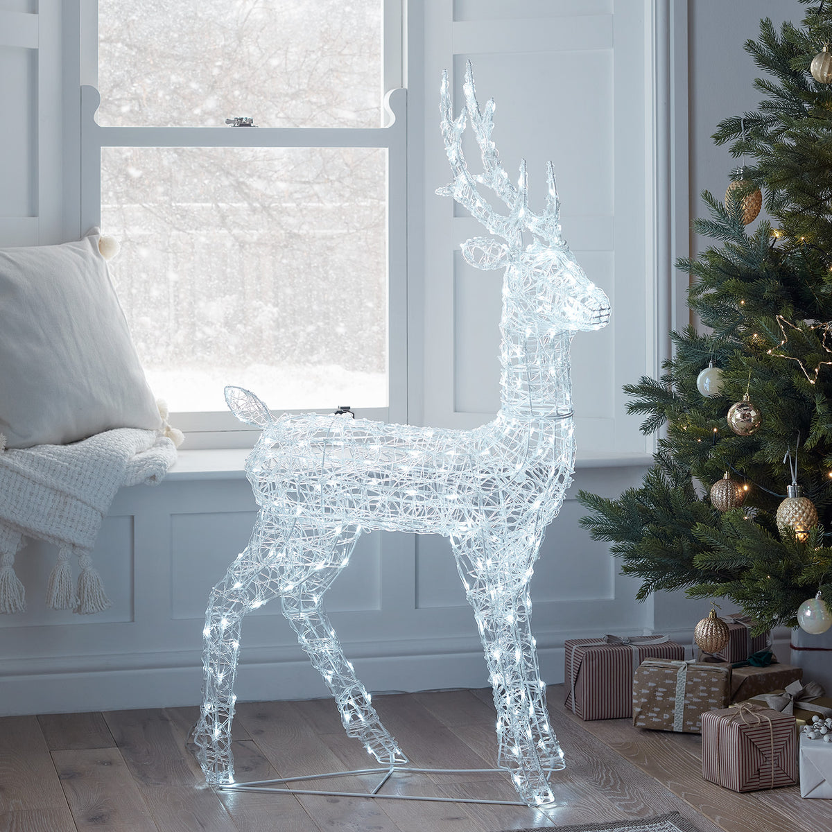 LED-Rentier in Innenraum neben Fenster und Weihnachtsbaum mit Geschenken