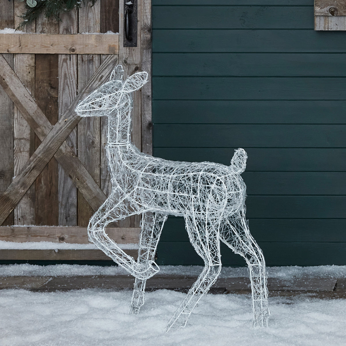 LED-Dekofigur Rehkitz aus weißem Acryl mit LED-Lichterkette im Schnee vor Holztür