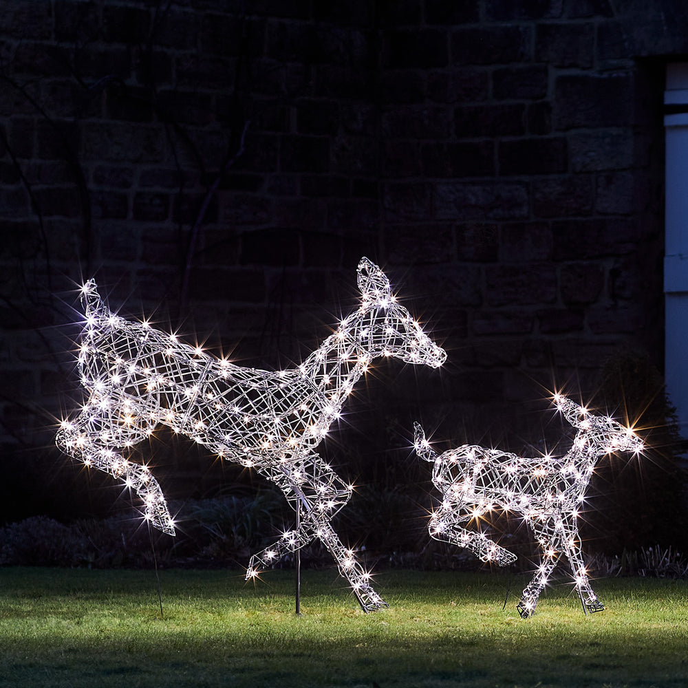 Zwei springende LED-Rentiere mit weißen Lichtern aus Rattanoptik im Garten bei Nacht