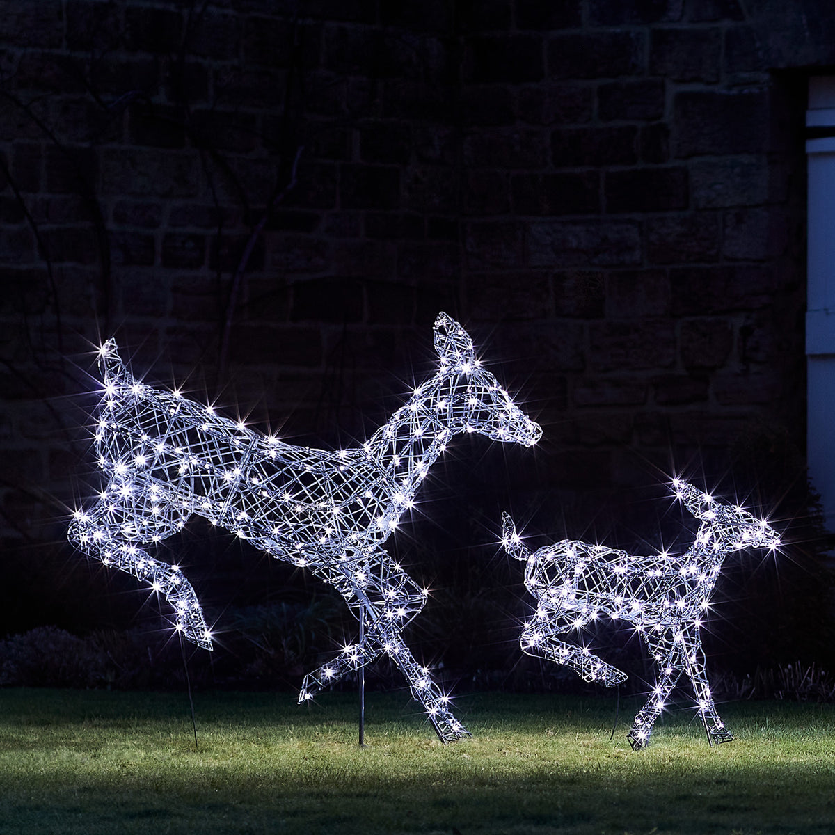 Zwei springende LED-Rentiere mit kaltweißen Lichtern aus Rattanoptik im Garten bei Nacht