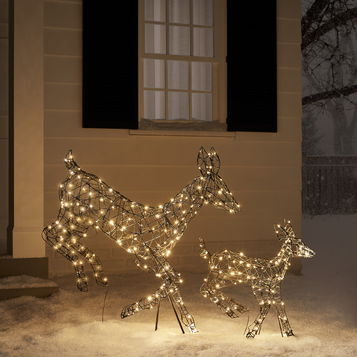 Zwei springende LED-Rentiere mit warmweißen Lichtern im Schnee vor einem Haus