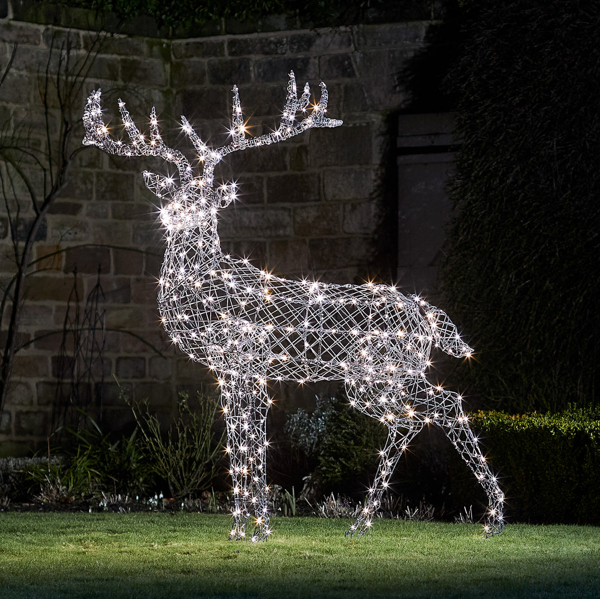 Große LED Rentierfigur mit weiß leuchtenden Lichtern aus Rattanoptik im Garten bei Nacht