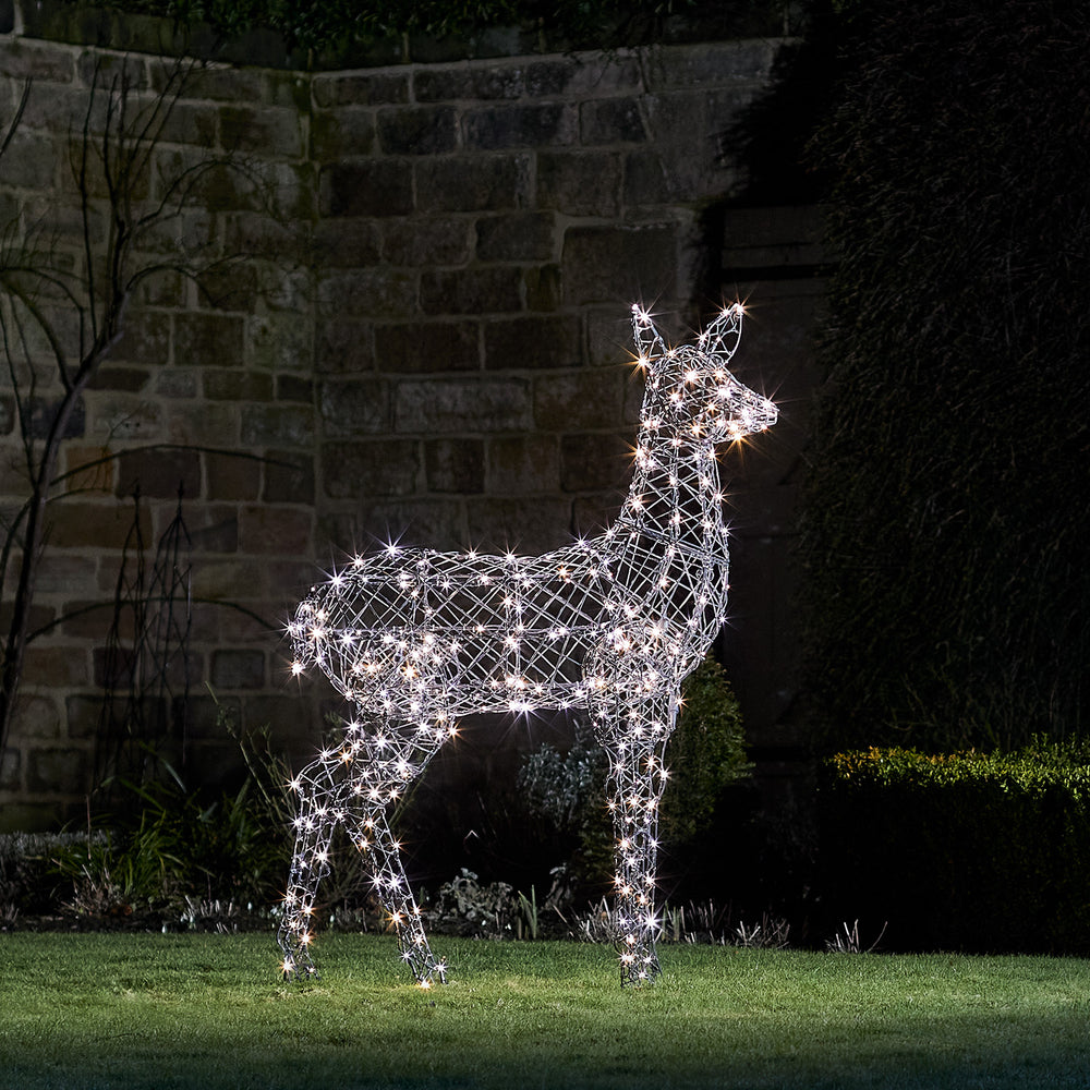 LED-Rentier Hirschkuh mit weiß leuchtenden LEDs im Garten vor einer Steinmauer bei Nacht