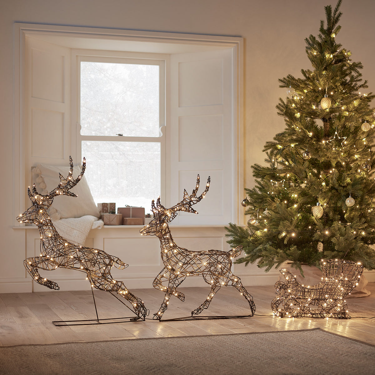 LED-Rentiere mit Schlitten aus Rattanoptik beleuchtet im Wohnzimmer neben Weihnachtsbaum