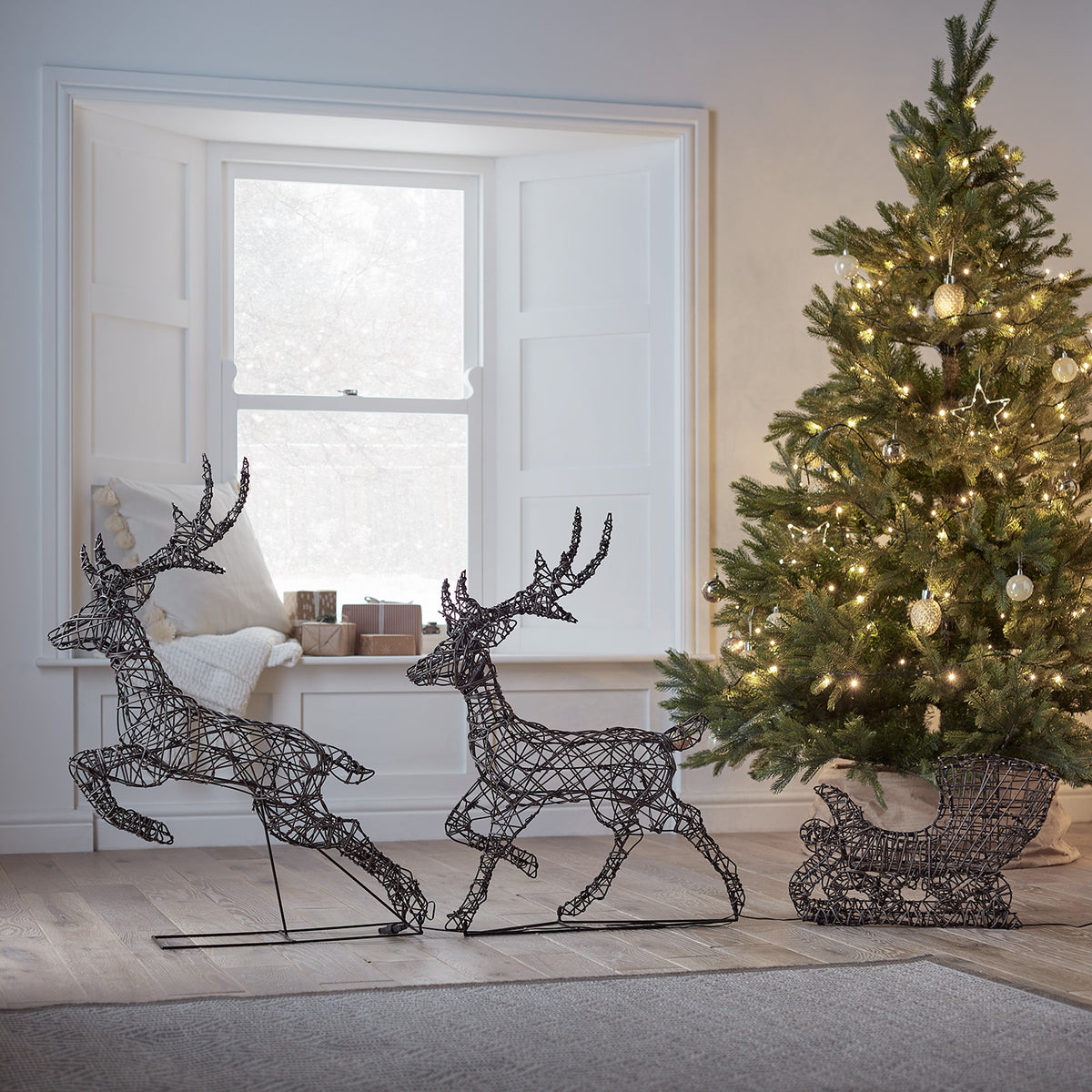 LED-Rentiere mit Schlitten aus Rattanoptik ohne Beleuchtung im Wohnzimmer neben Weihnachtsbaum